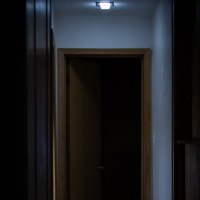Very dark image of a dimly lit hallway with someone lying down on their stomach